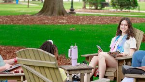 Happy student sits in a circle of chairs on the quad, while studying outside on a beautiful summer day.