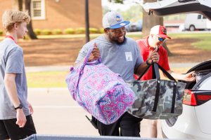UAEC Staff member assists student and parent with bags during Summer On Campus move in.