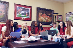 Eight students study and laugh together on a large couch, with many Alabama football prints on the wall