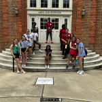 Twelve smiling LEAP students have fun posing together in the shape of an A, on the front steps of Clark Hall, on The University of Alabama campus.